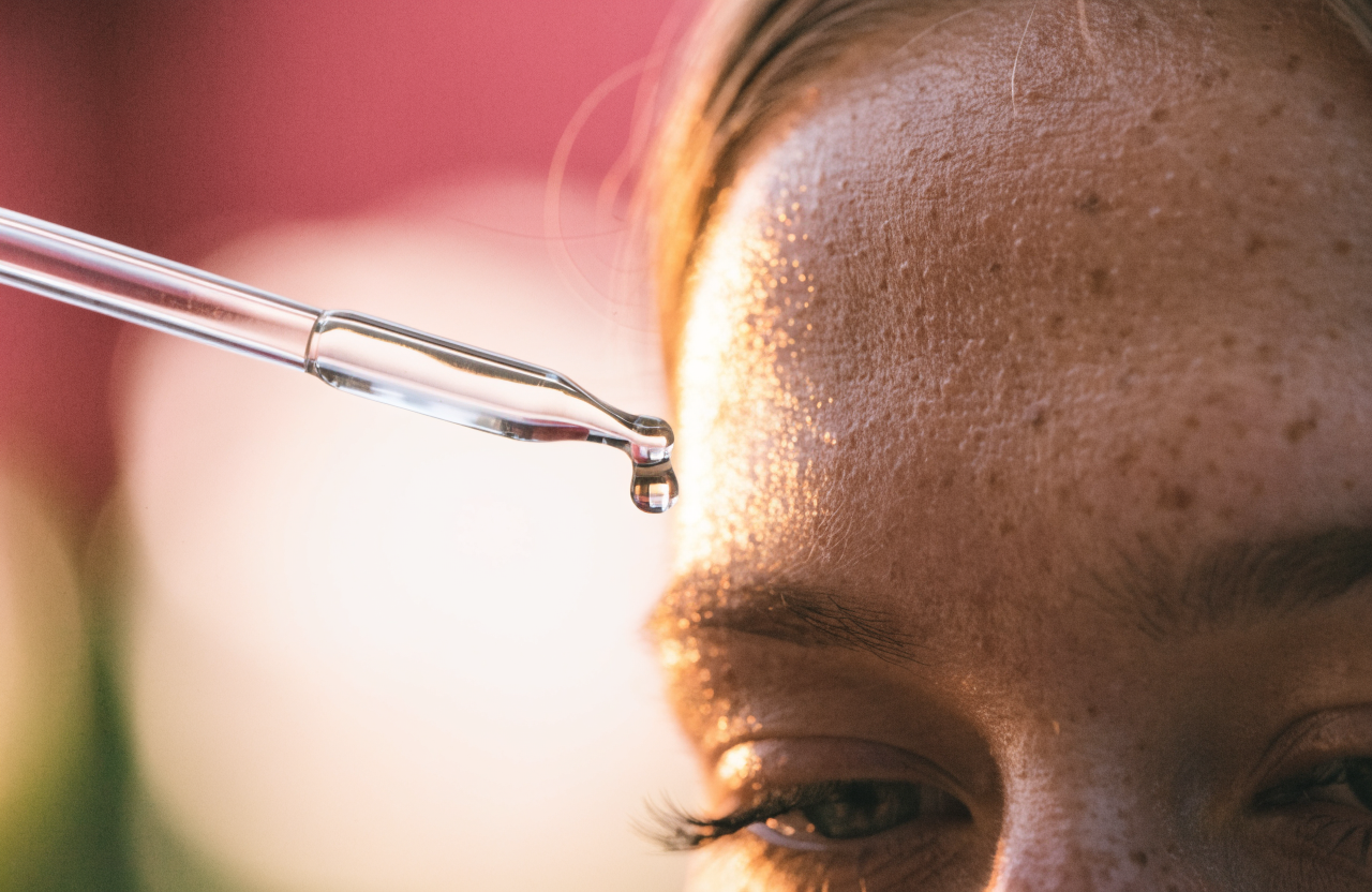 A glass pipette holding a single clear drop above freckled skin.