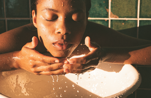Water cupped to the face at a basin in warm evening light.