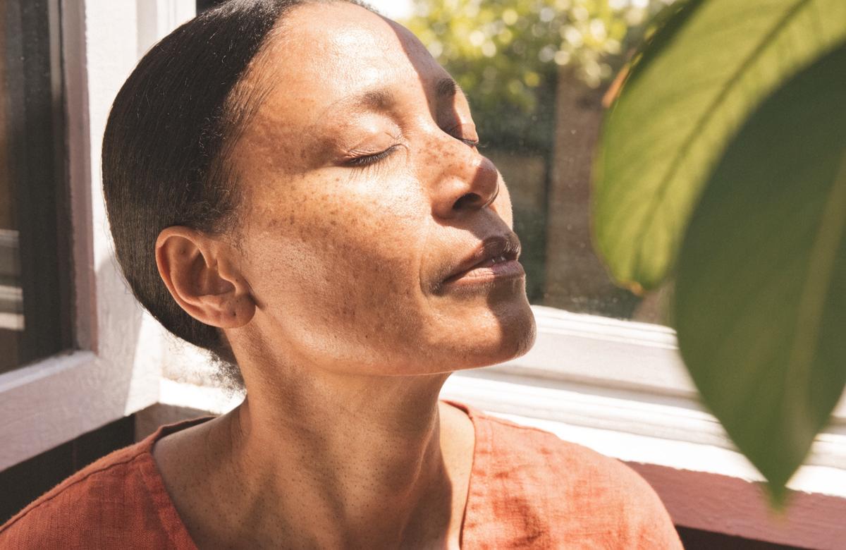 A woman with her face turned into strong morning sun at an open window.