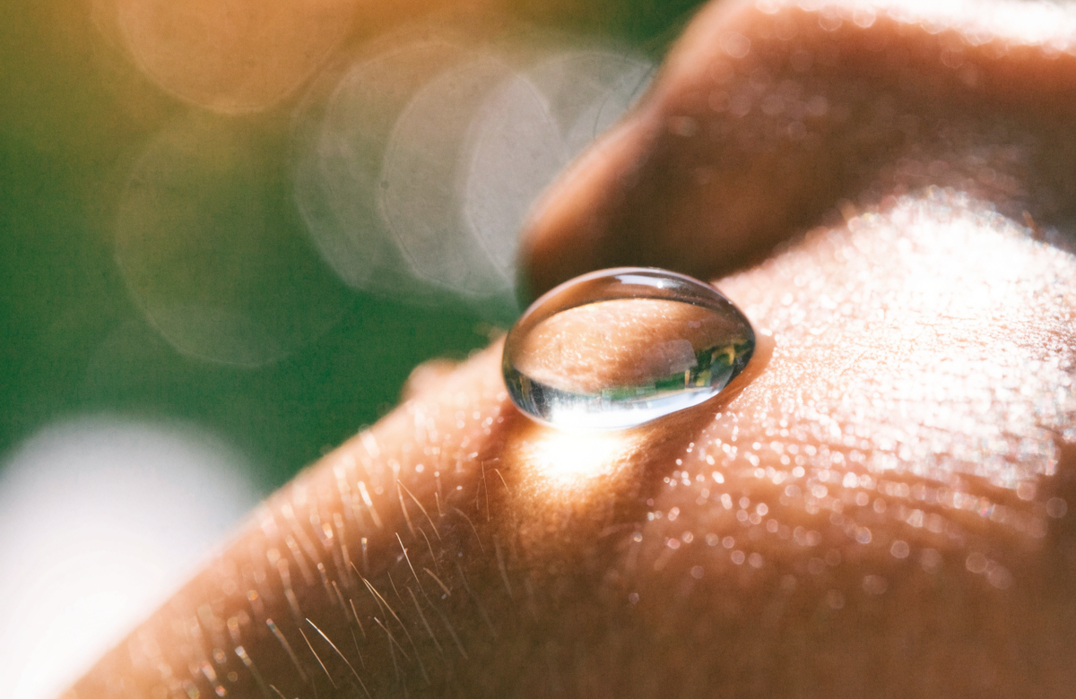 A single drop of serum resting on the skin of a cheekbone.