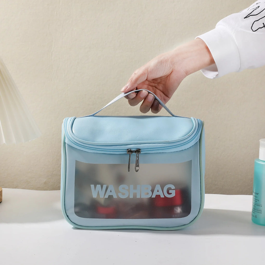 A hand lifting the blue frosted washbag by its handle