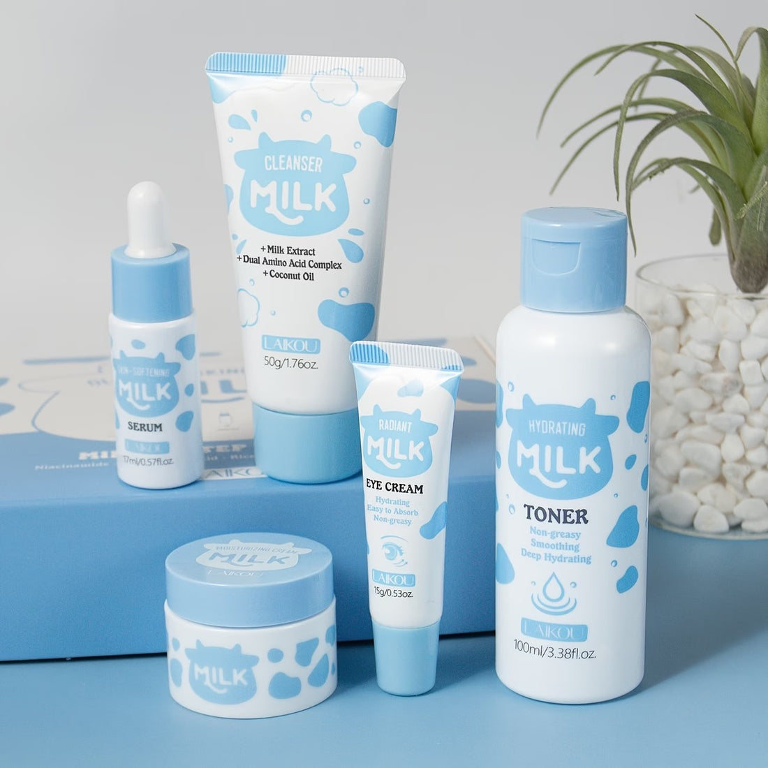 The Milk five-piece set on a blue plinth beside a plant and a jar of white pebbles.